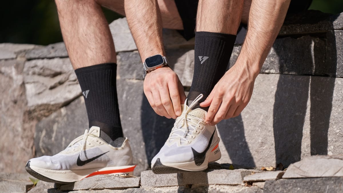 Man wearing an Apple Watch tying his running shoes on stone steps outdoors
